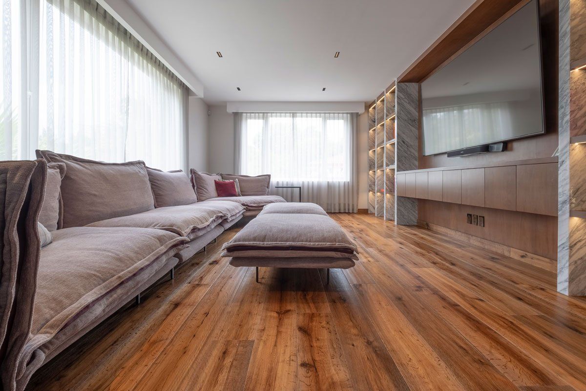 Sala de estar moderna con sofá modular gris, suelo de madera, televisor grande y luz natural proveniente de la ventana.