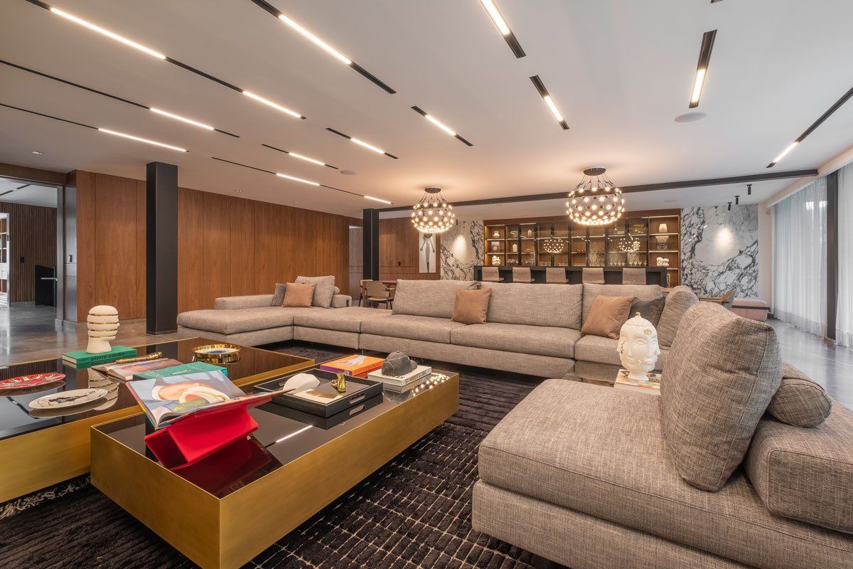 Sala de estar moderna con sofás seccionales beige, mesas de centro, revestimiento de madera y lámparas colgantes.