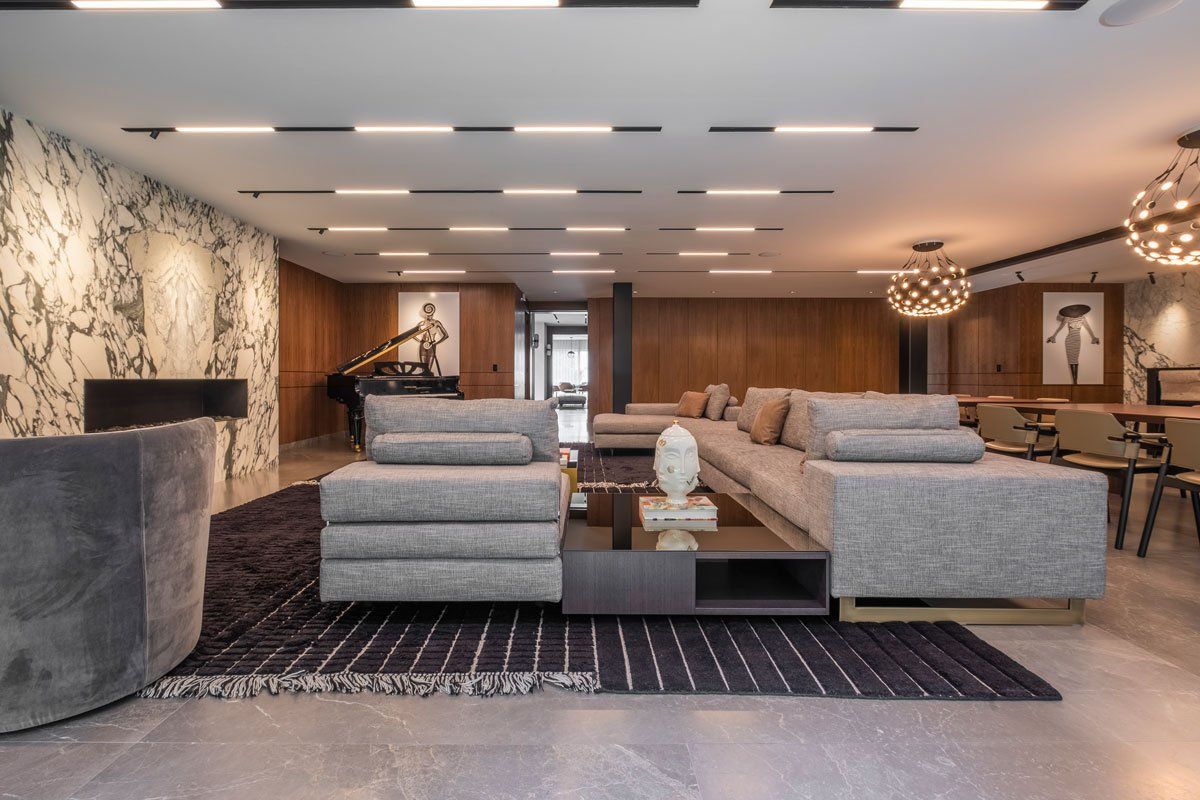 Salón moderno con sillones grises, sofá, chimenea, paredes revestidas de madera y alfombra estampada.