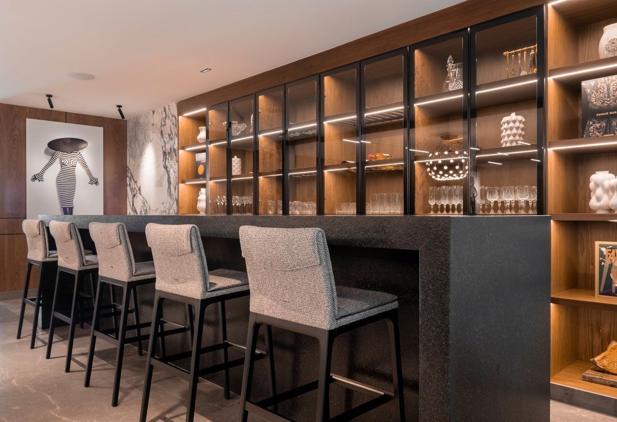 Bar moderno con estantes retroiluminados, taburetes y obras de arte enmarcadas en la pared en un interior cálido.