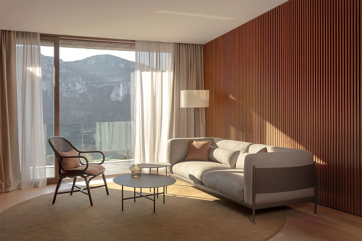 Sala de estar moderna con sofá gris, sillón, mesa de centro y vista a la montaña a través de grandes ventanales.