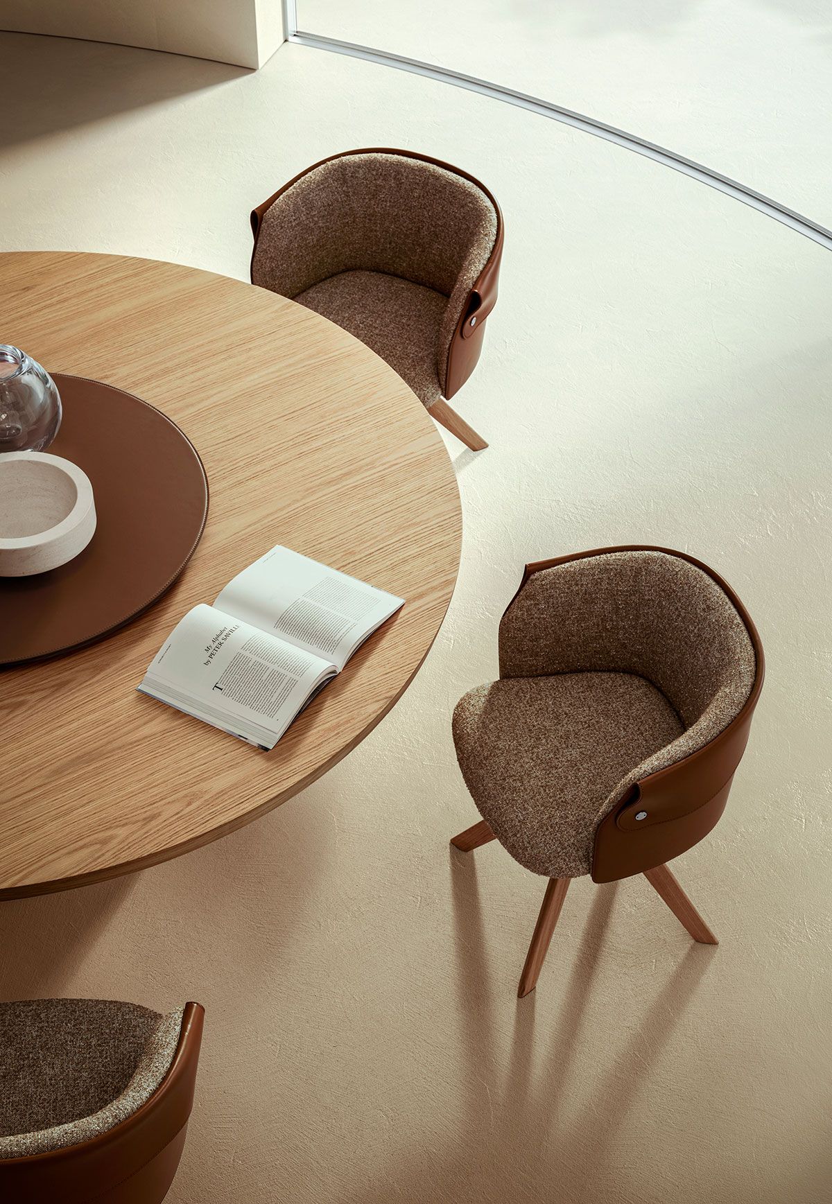 Una mesa redonda con sillas en una habitación luminosa, con tazas y un libro abierto.