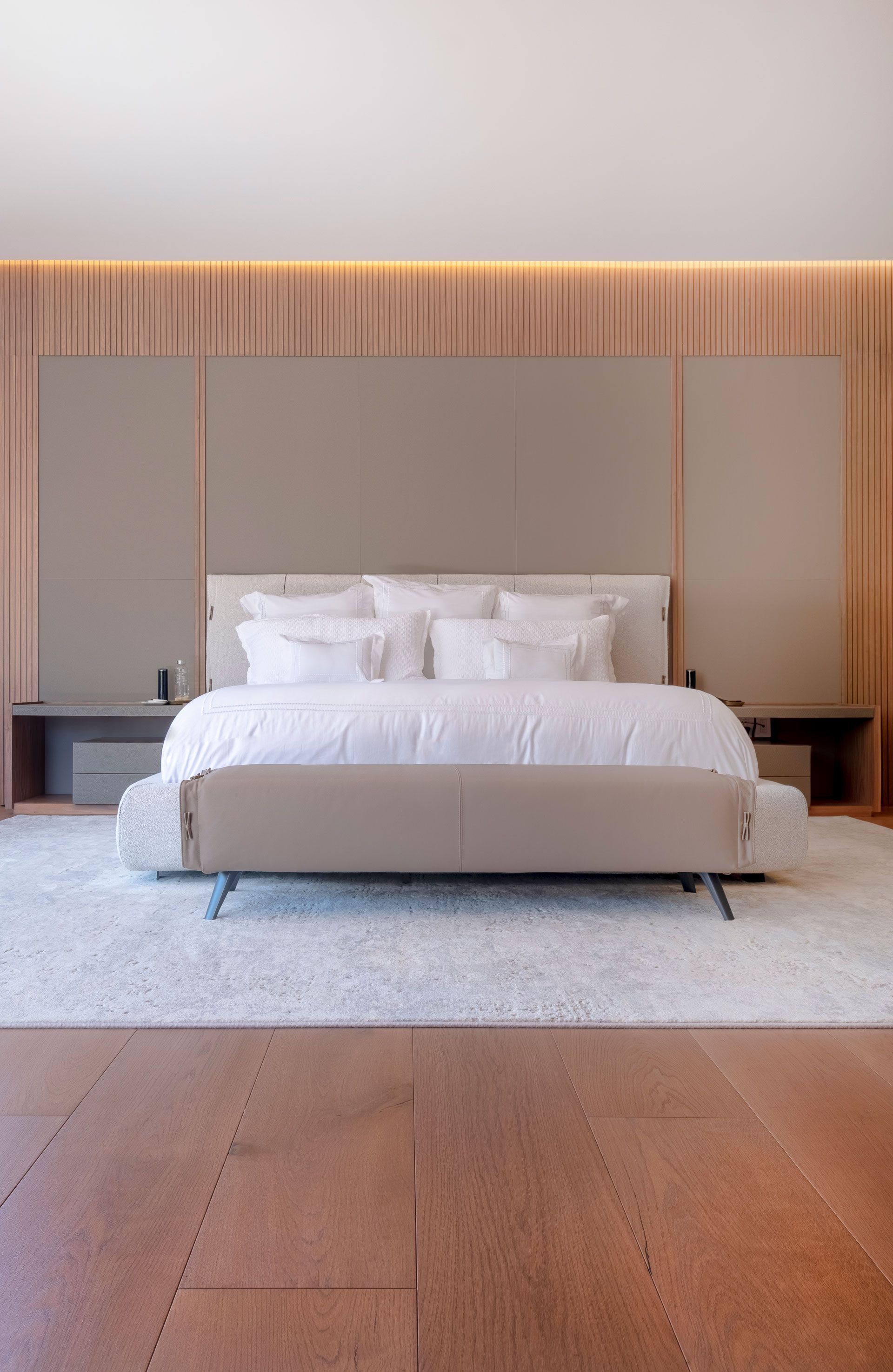 Dormitorio minimalista con cama blanca, pared revestida de madera y decoración suave en tonos neutros.