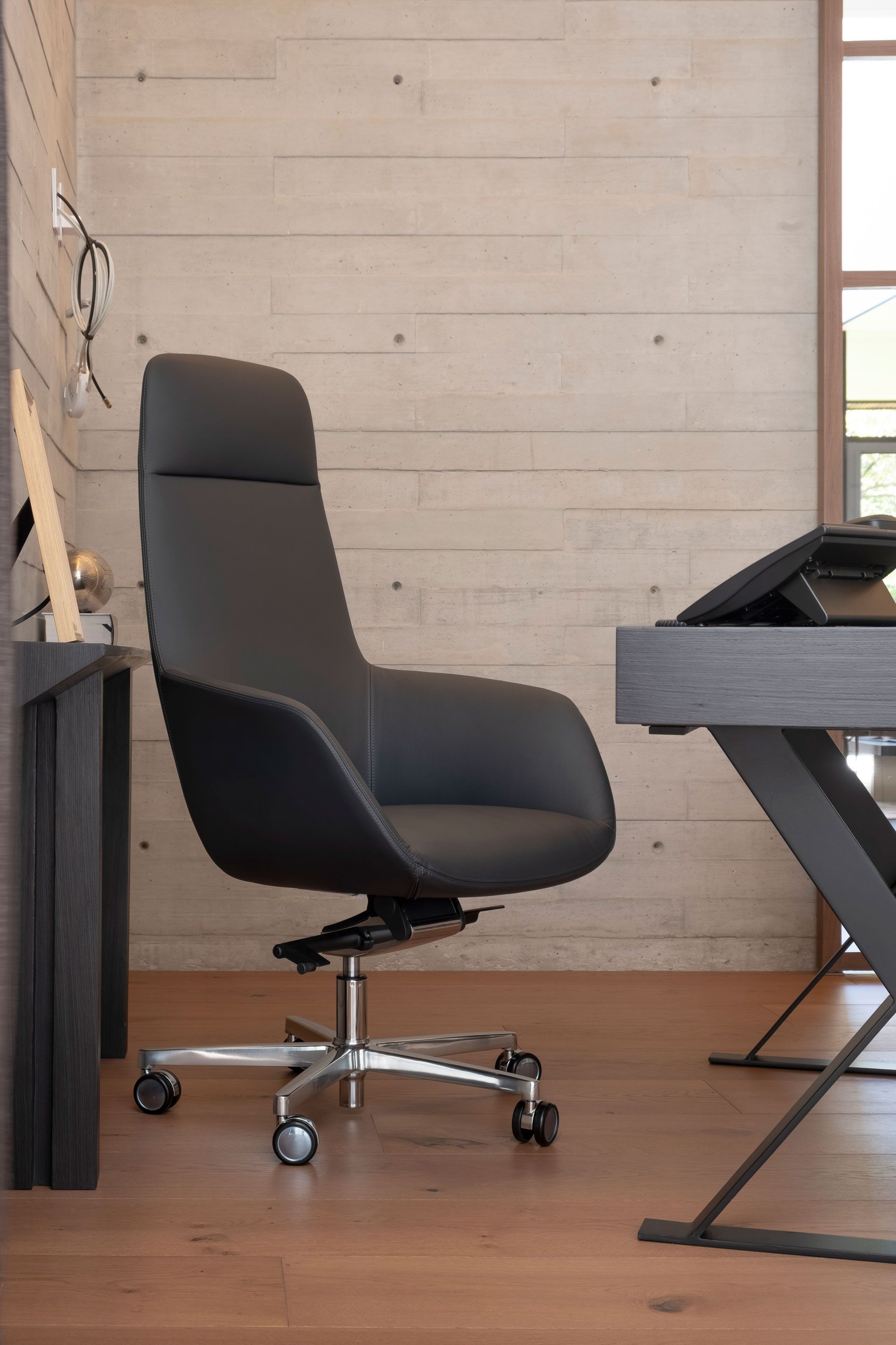 Silla de oficina negra con ruedas junto a un escritorio en una habitación moderna.