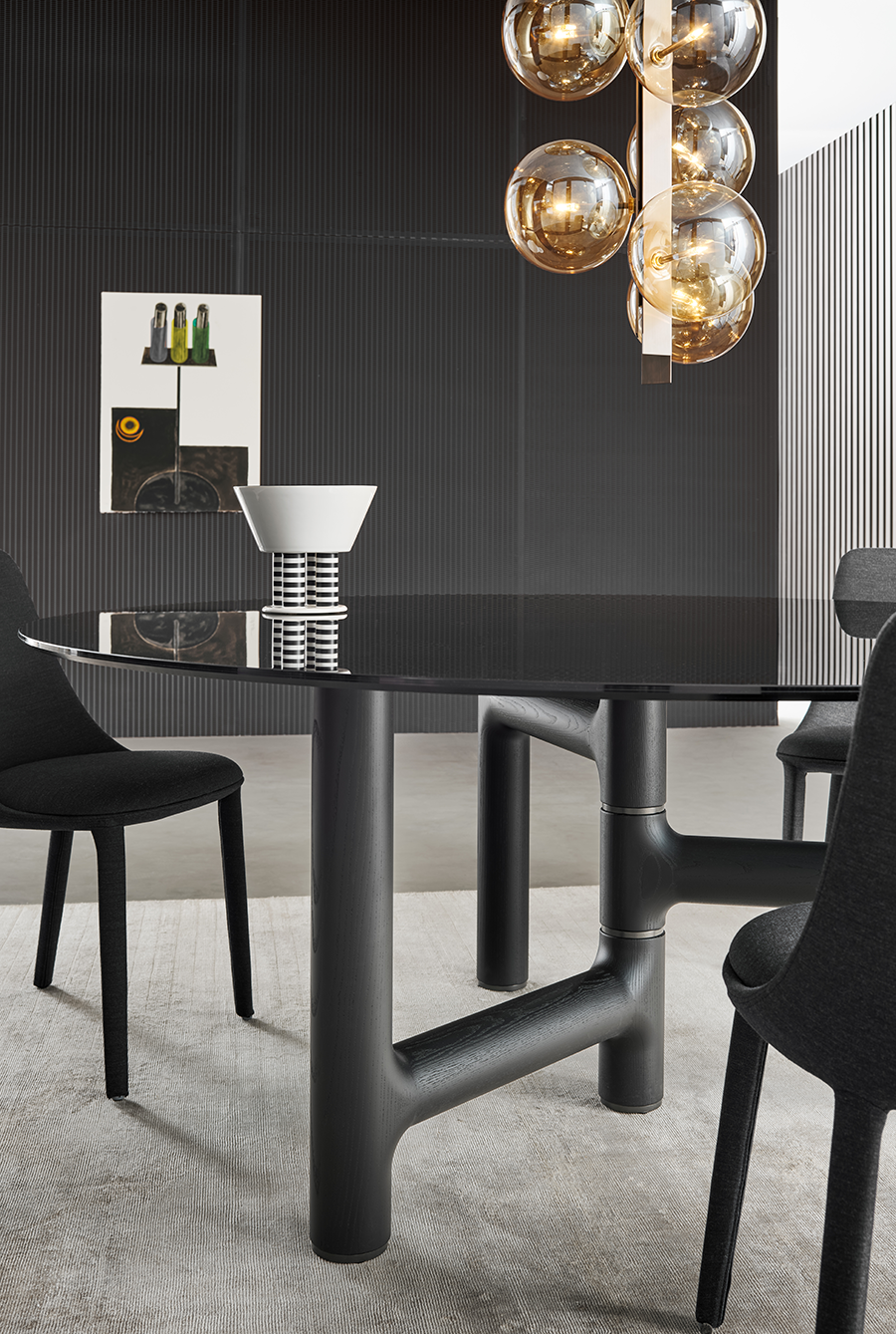 Comedor moderno con mesa, sillas y lámparas colgantes negras, y pared acanalada oscura.