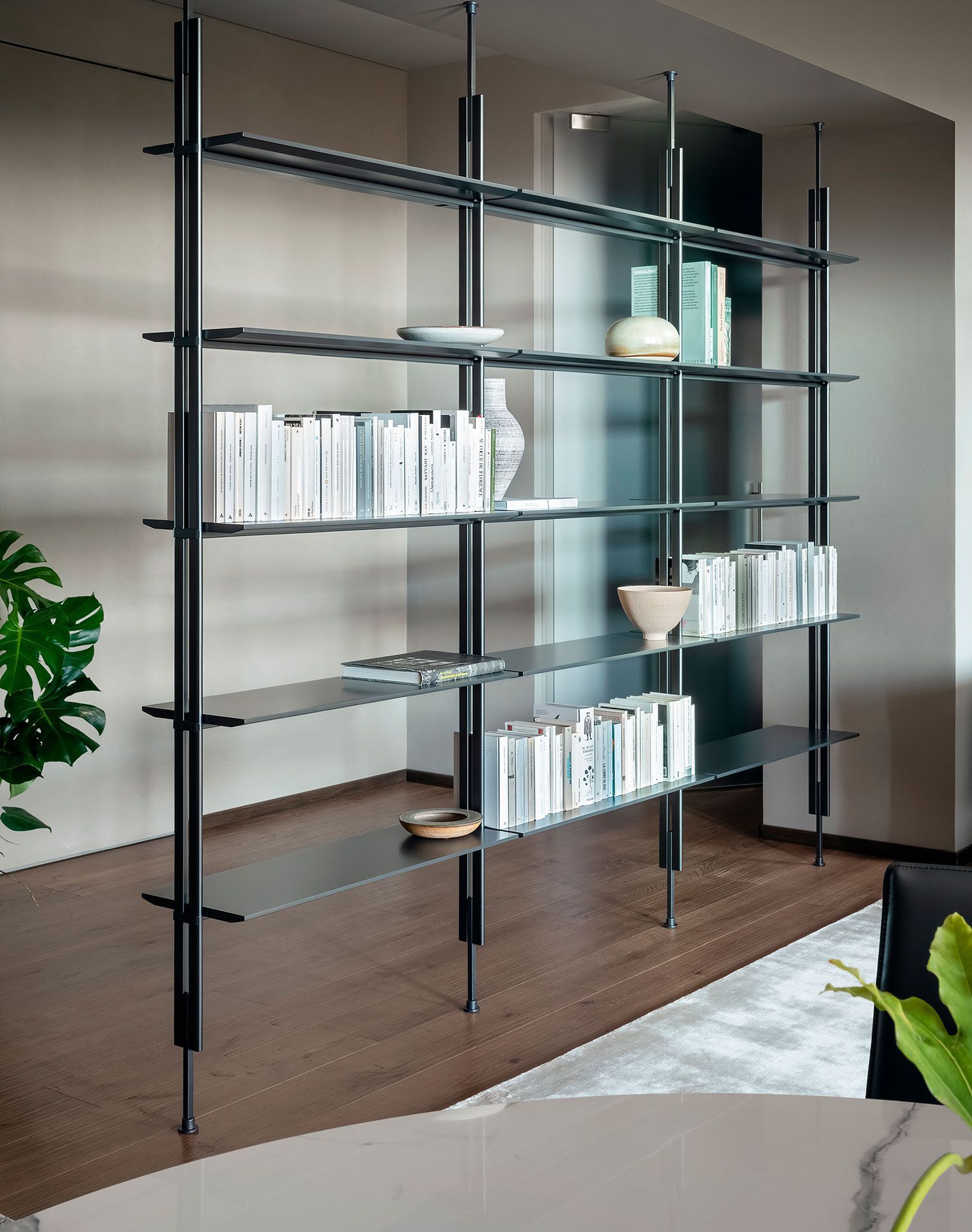 Estanterías modernas de metal negro con libros y elementos decorativos en una sala de estar minimalista.