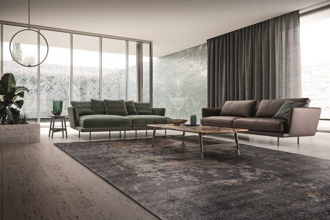 Modern living room with a green sofa, gray loveseat, large windows, sheer curtains, and a dark area rug.