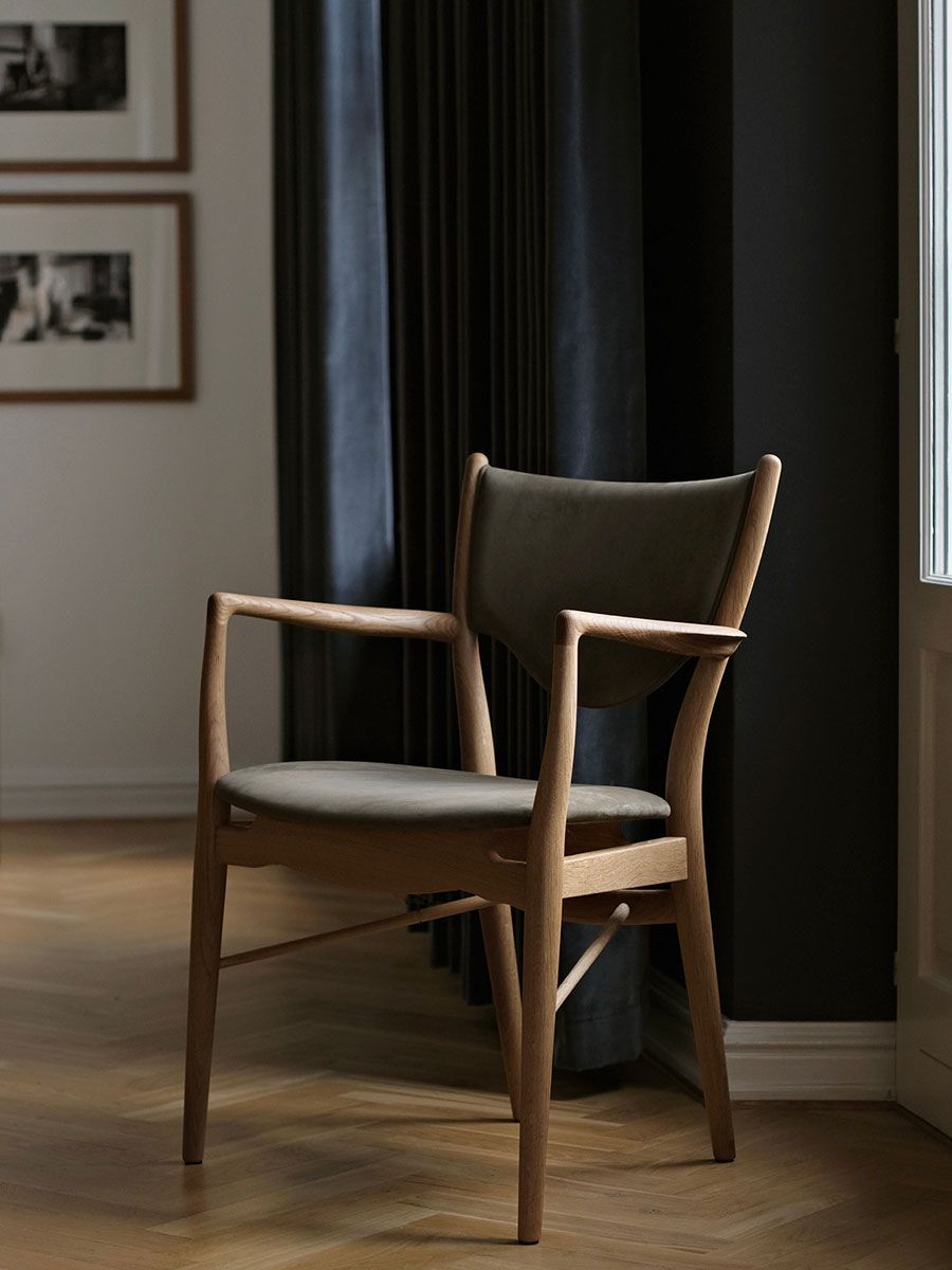 Sillón moderno de madera con cojín gris junto a cortinas oscuras en una habitación minimalista.