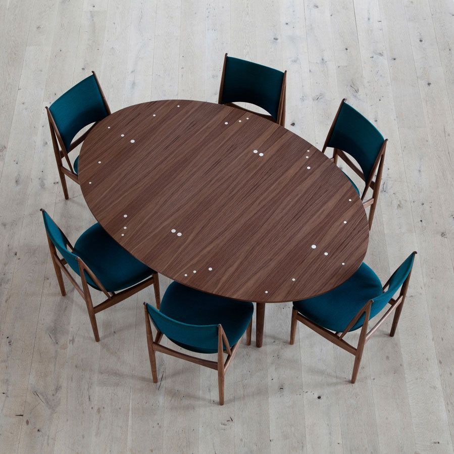 Mesa redonda de madera rodeada de seis sillas de color verde azulado sobre un suelo claro.