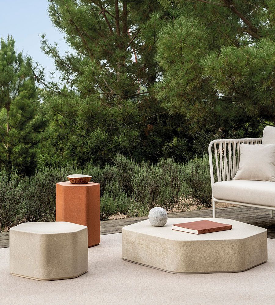 Patio exterior minimalista con asientos de color beige, mesa de terracota y fondo vegetal.