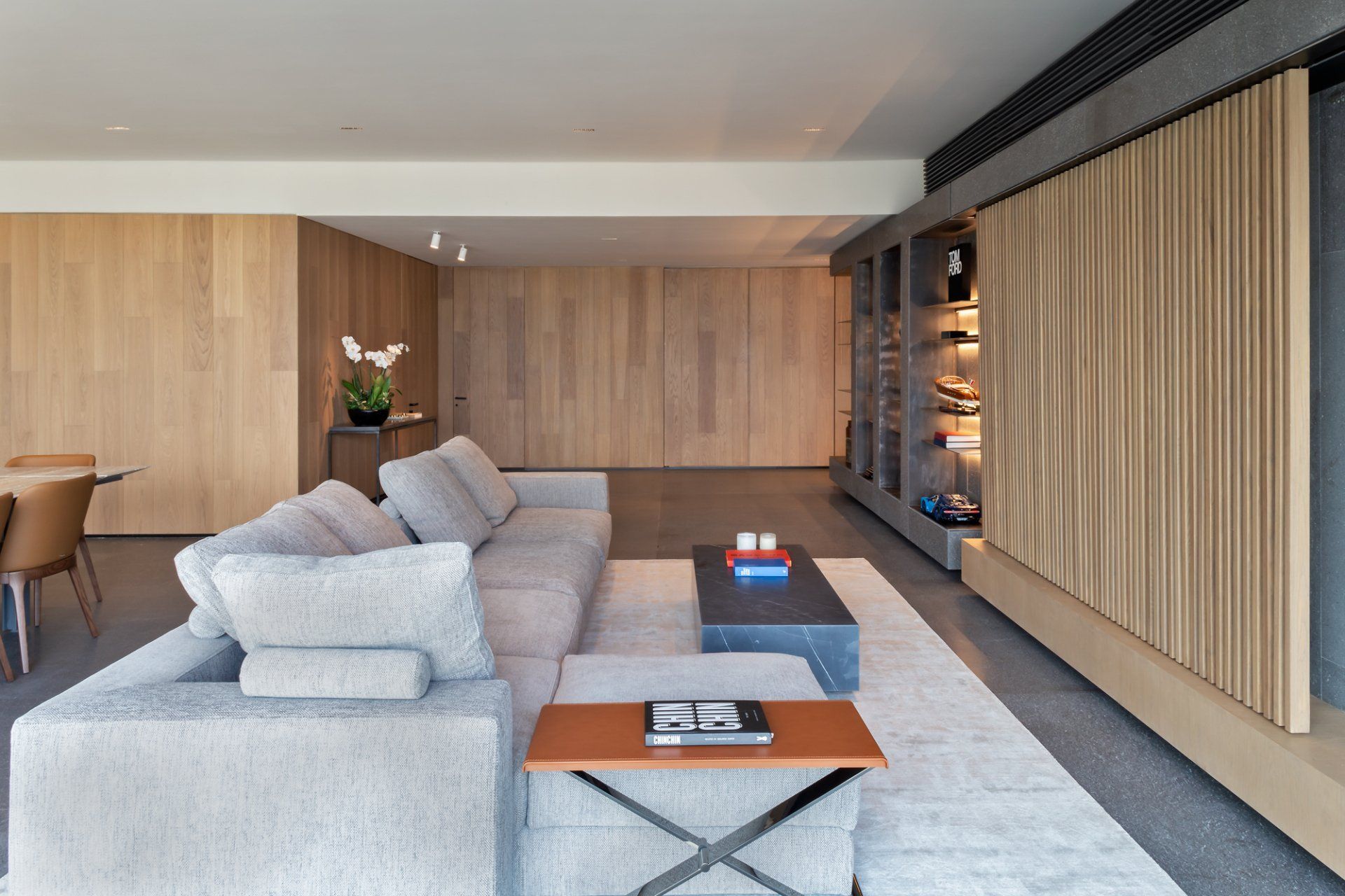 Salón moderno con sofá gris, revestimiento de madera y grandes paneles divisorios corredizos de madera.