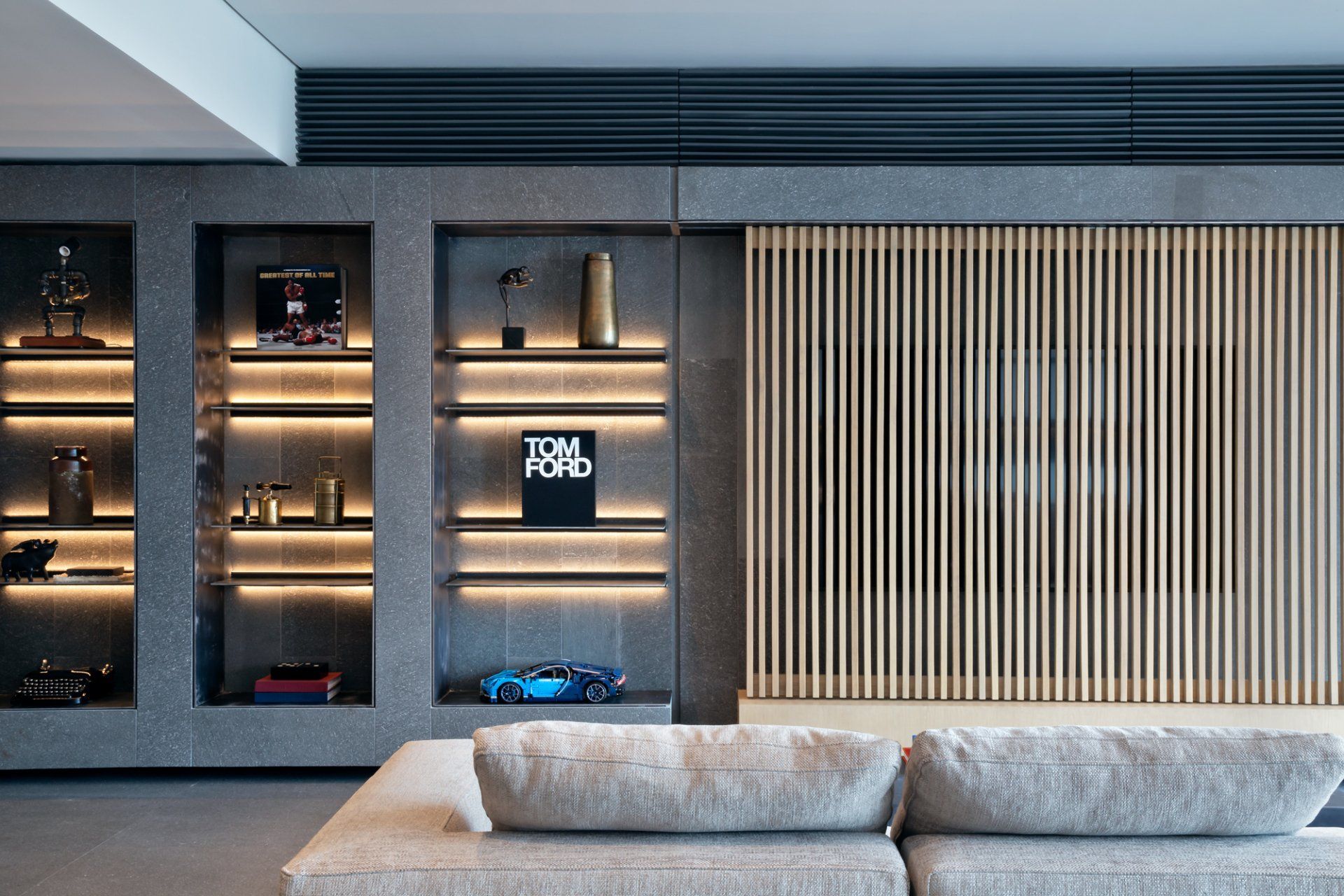 Sala de estar moderna con estantes iluminados empotrados, listones de madera verticales y un sofá gris claro.