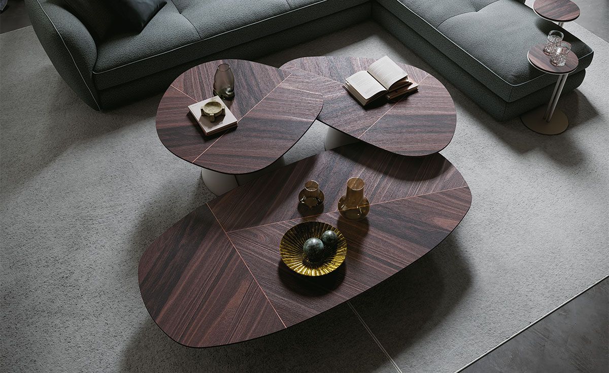 Mesa de centro moderna colocada sobre un sofá gris en una sala de estar, con libros y un jarrón decorativo encima.