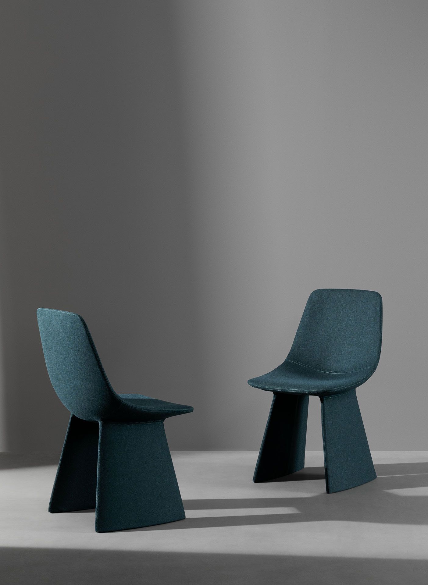 Dos sillas modernas de color verde azulado en una habitación minimalista gris con sombras suaves.