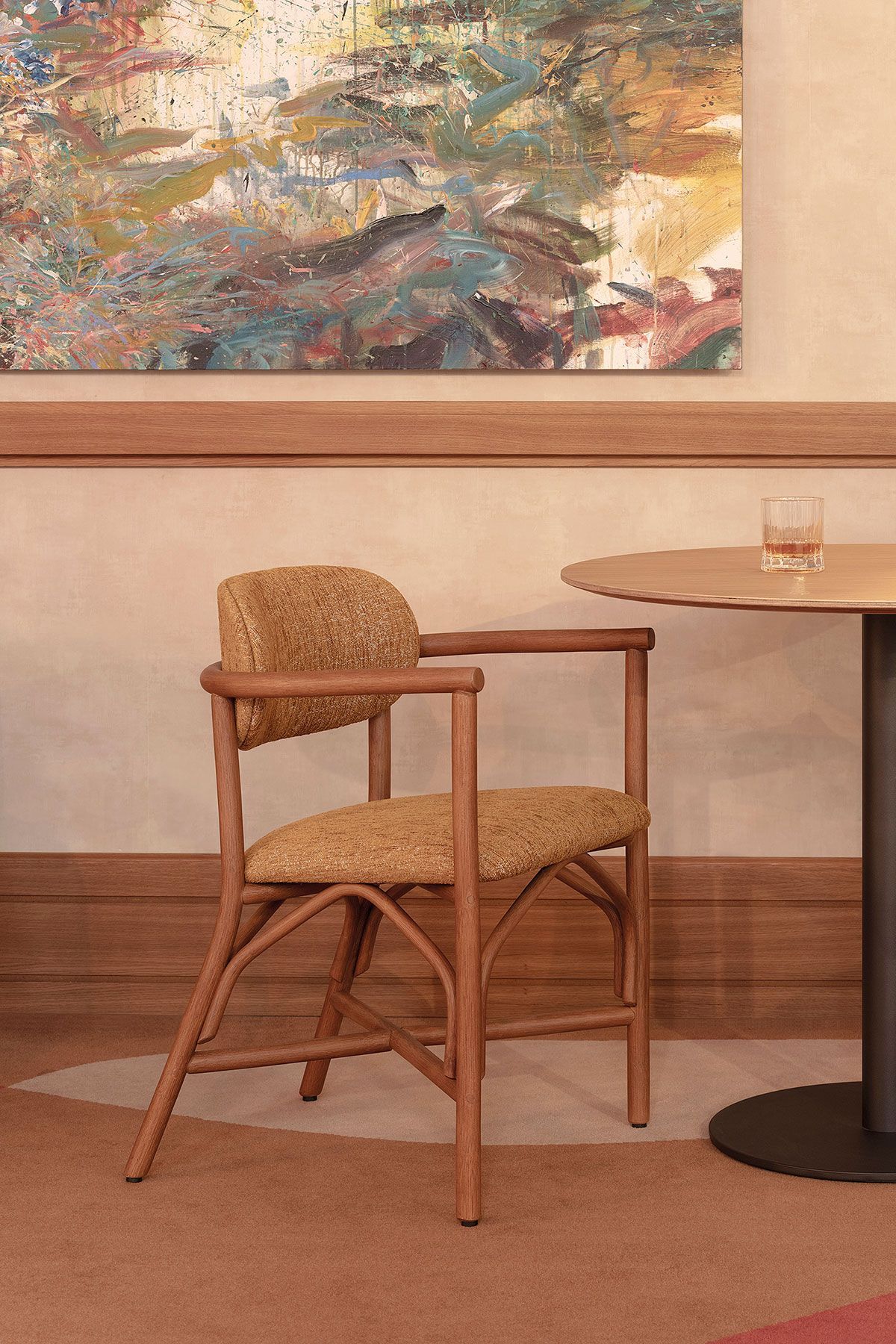 Silla de mimbre junto a una pequeña mesa redonda en una cafetería, con un colorido cuadro abstracto en la pared.