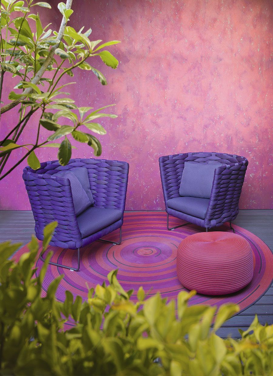 Sillas de patio moradas y alfombra en un patio rosa con plantas en primer plano.