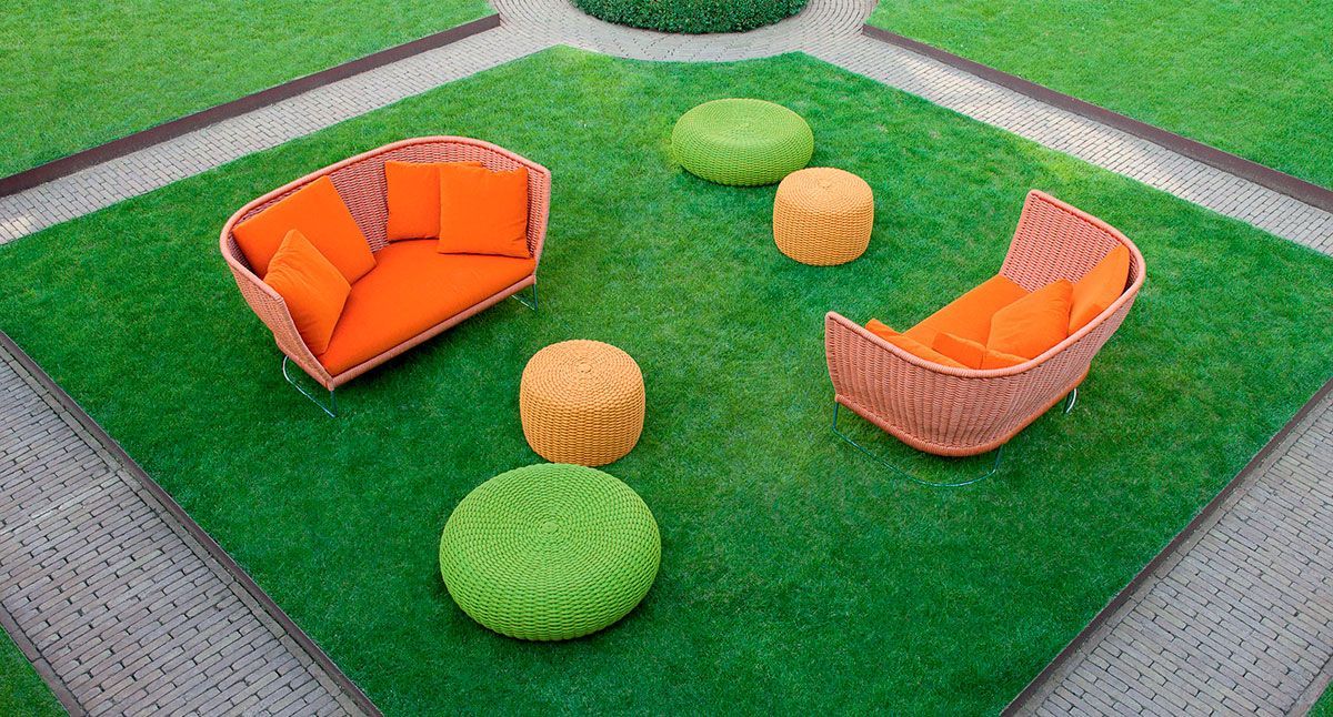 Patio exterior con dos sofás naranjas y otomanas redondas verdes y naranjas sobre césped artificial.