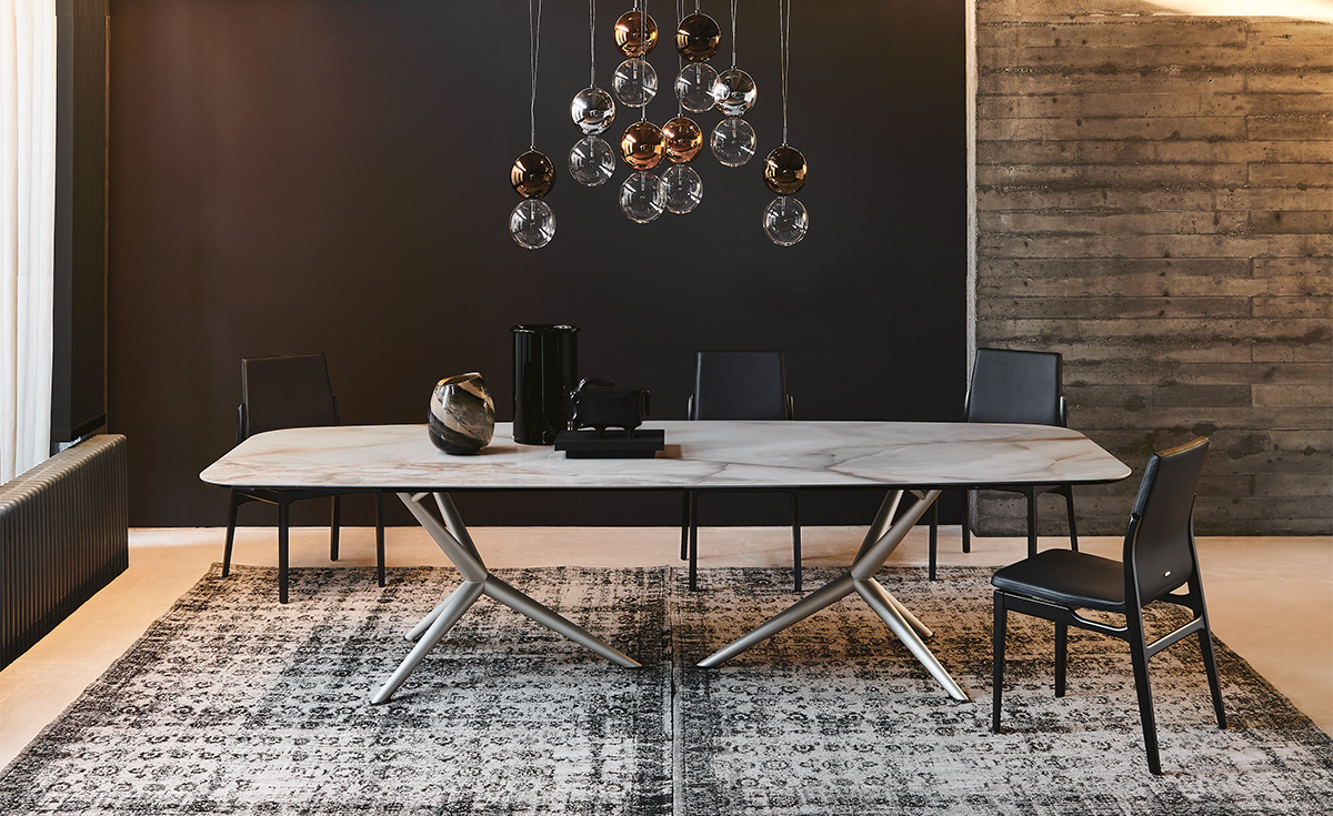 Comedor moderno con mesa larga de madera, sillas negras, lámparas colgantes y alfombra estampada.