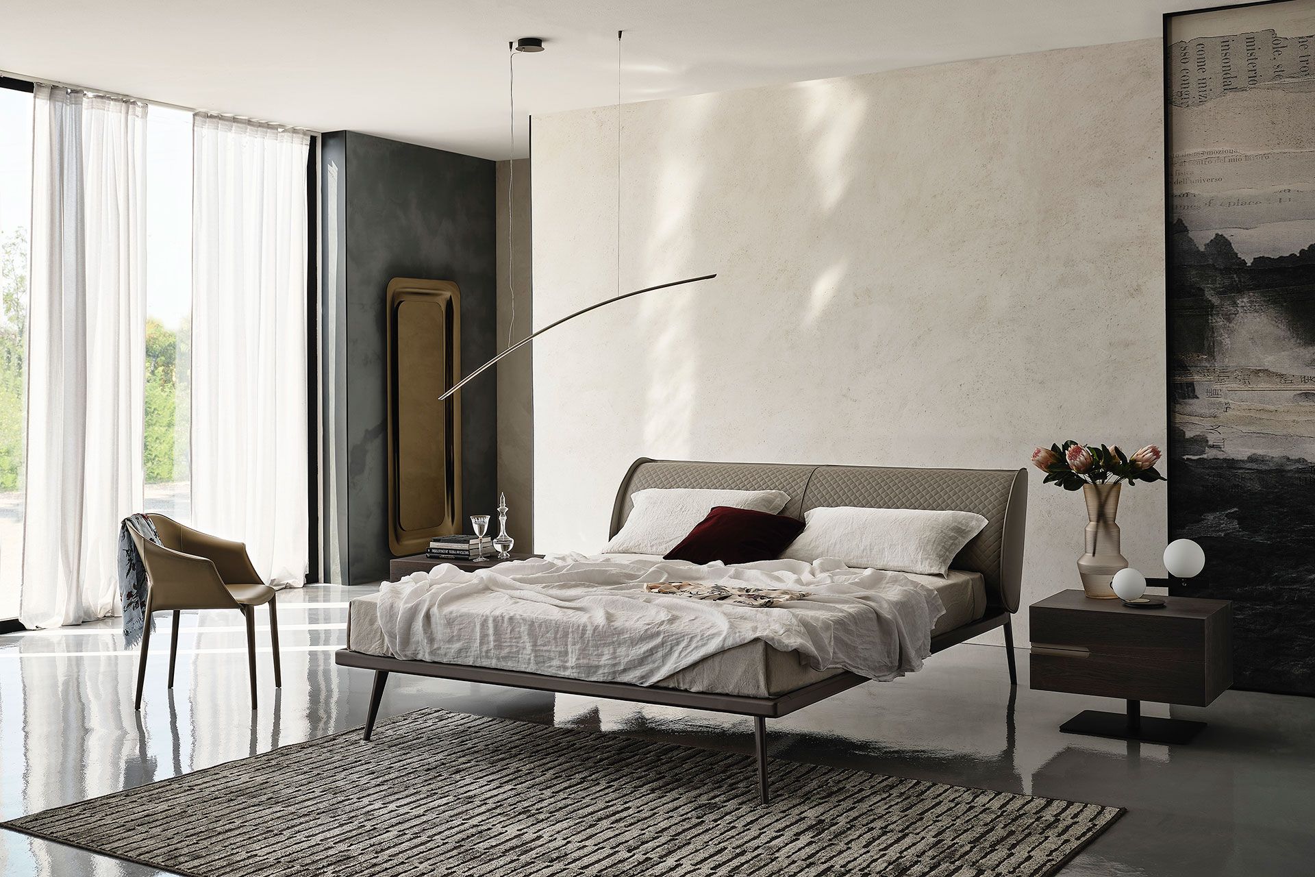 Dormitorio moderno con cama baja, paredes blancas, ventana grande, silla y alfombra estampada.
