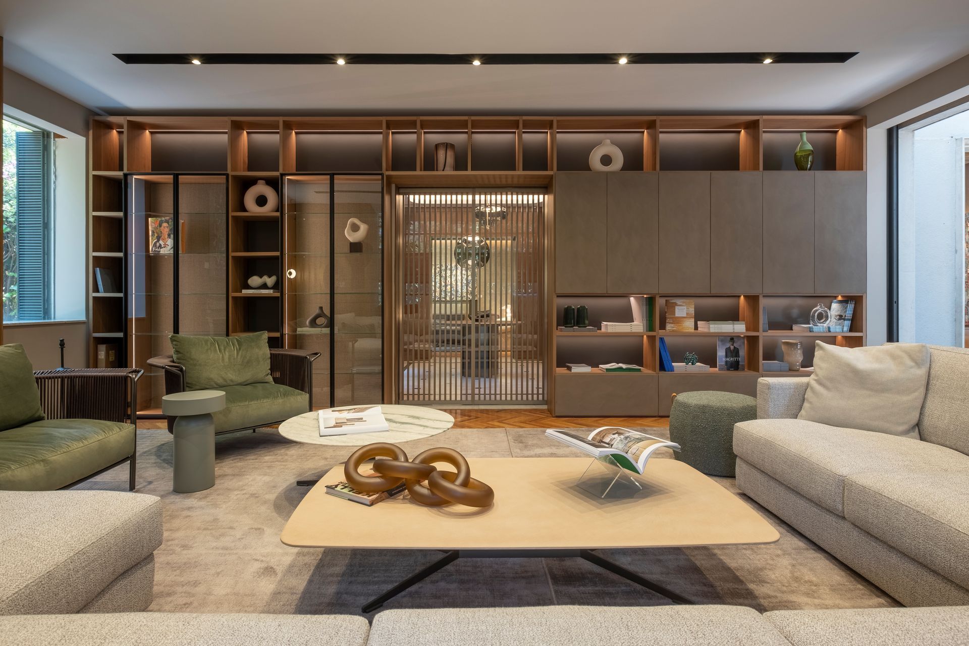 Sala de estar moderna con sofás grises, sillas verdes, estanterías de madera y una mesa de centro.