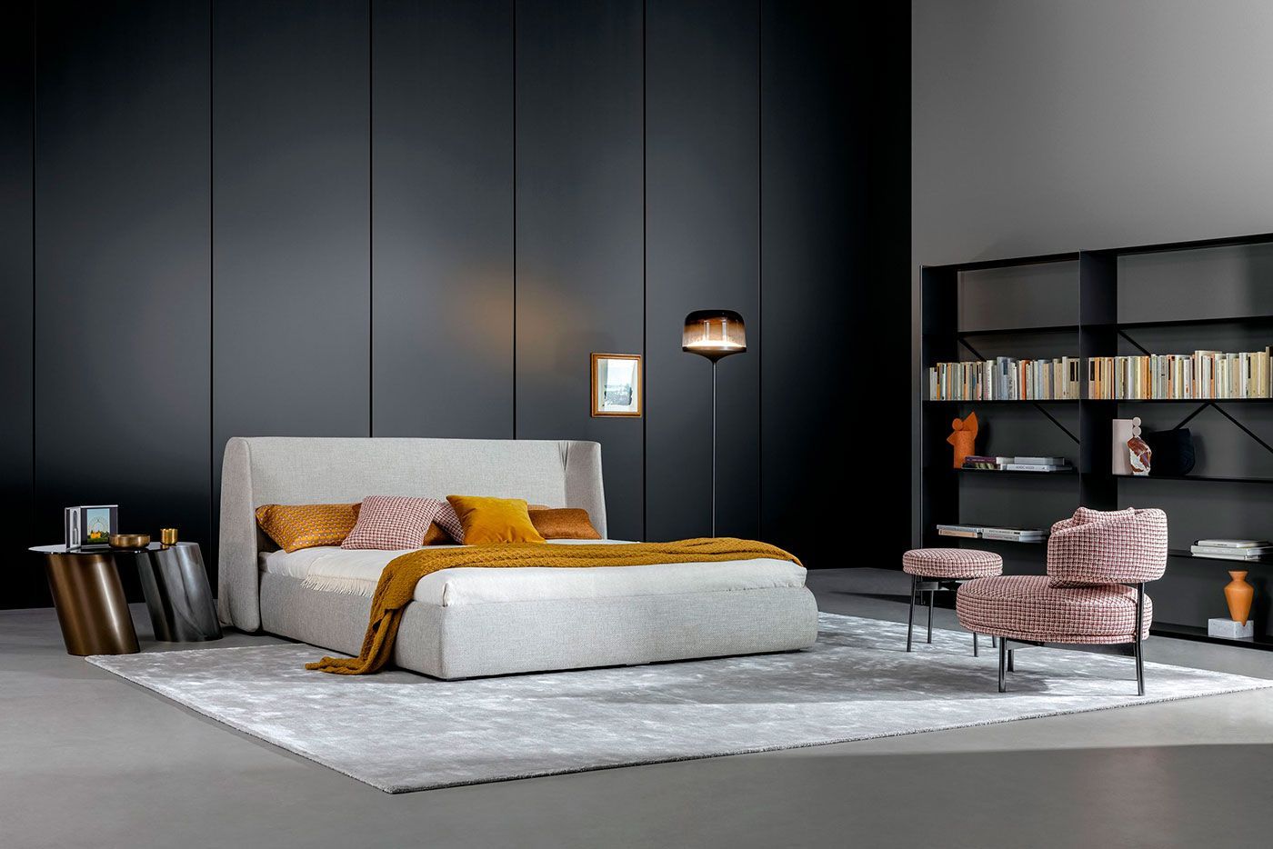 Dormitorio moderno con paredes oscuras, cama blanca, manta color mostaza, sillón y estantería.