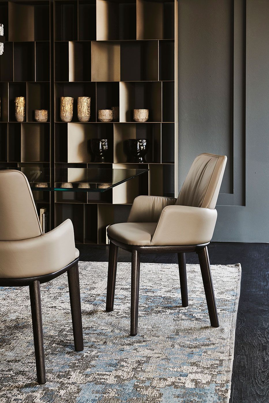 Dos sillas de color beige sobre una alfombra estampada en una habitación moderna de tonos oscuros con estanterías