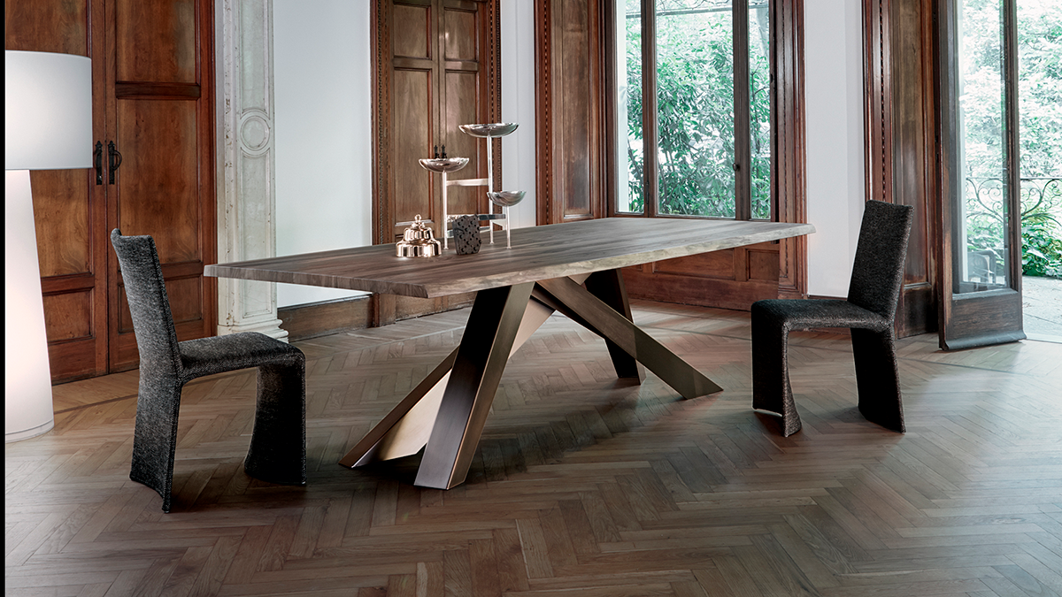 Comedor moderno con una mesa rústica de madera y dos sillas de mimbre oscuro junto a grandes ventanales.
