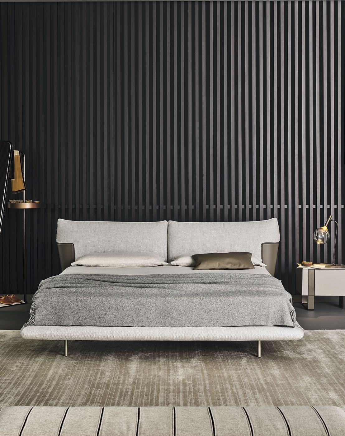 Dormitorio moderno con cama gris, pared decorativa a rayas oscuras y mesitas de noche a juego con lámparas.