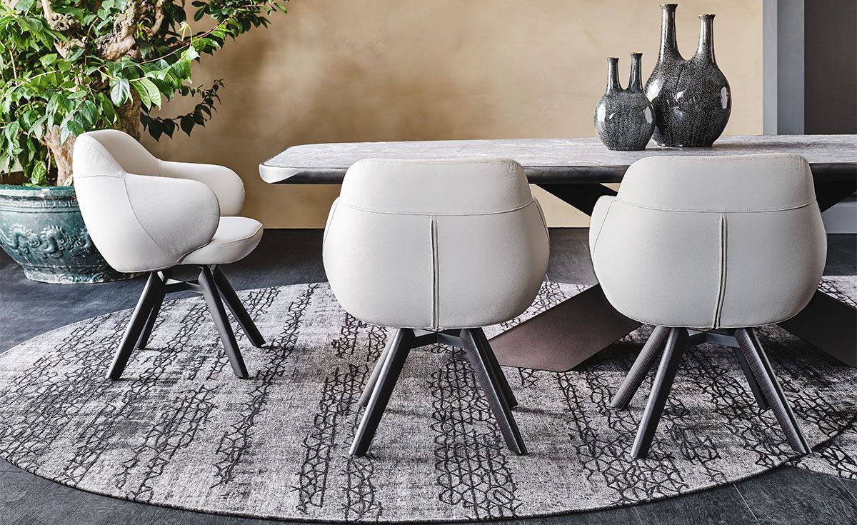 Comedor moderno con sillas blancas alrededor de una mesa redonda sobre una alfombra estampada y jarrones decorativos