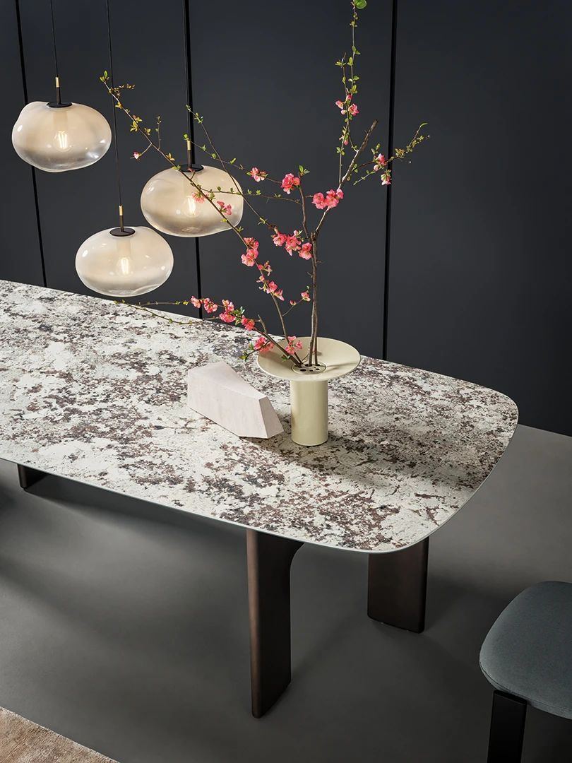 Mesa de mármol con lámparas colgantes y un jarrón con flores rosas sobre un fondo oscuro.