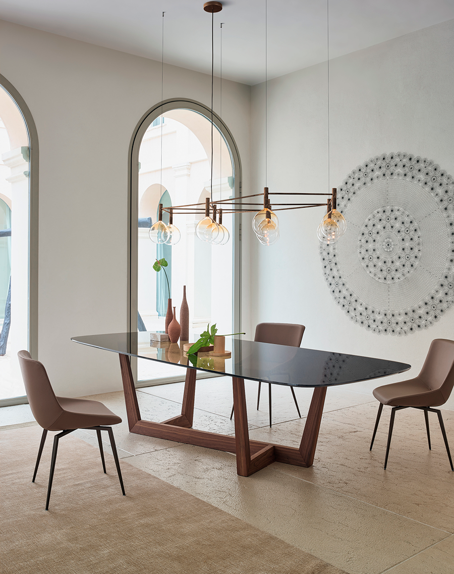 Comedor moderno con mesa de cristal, cuatro sillas, lámparas colgantes y espejos decorativos en la pared.