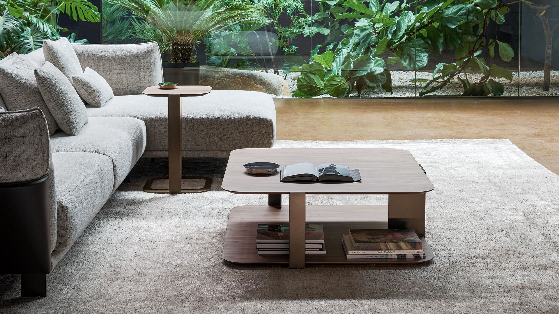 Moderna zona de estar en el patio con sofá gris, mesa de centro de madera y un exuberante jardín verde de fondo.