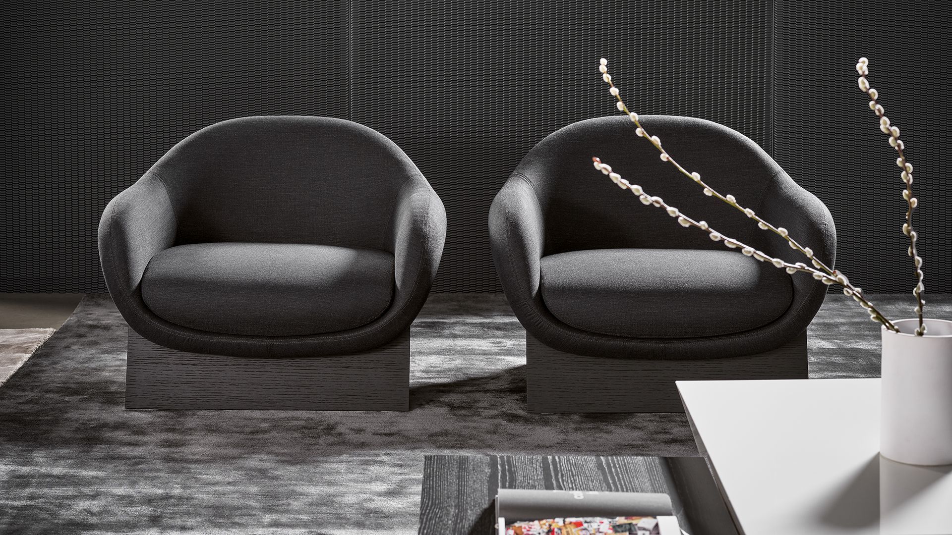 Dos sillones redondos de color gris oscuro sobre una alfombra en una sala de estar moderna, junto a una mesa blanca