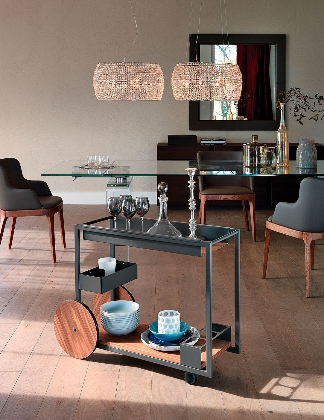 Comedor moderno con mesa de cristal, lámparas colgantes tejidas y un carrito de servicio negro con platos.