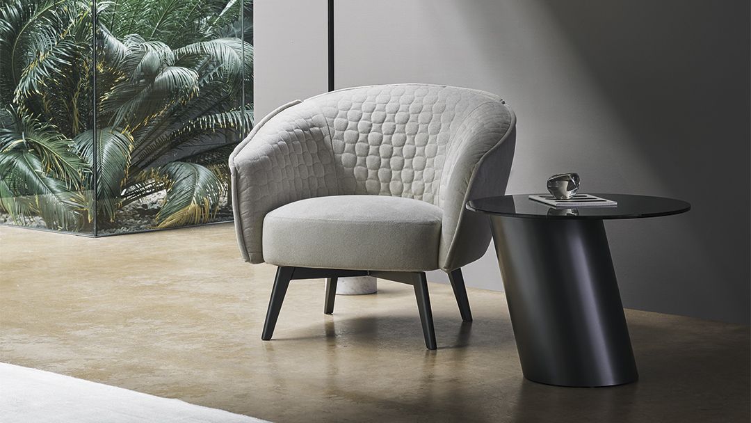 Sillón moderno gris junto a una mesa auxiliar negra en una habitación minimalista con vistas a la vegetación.