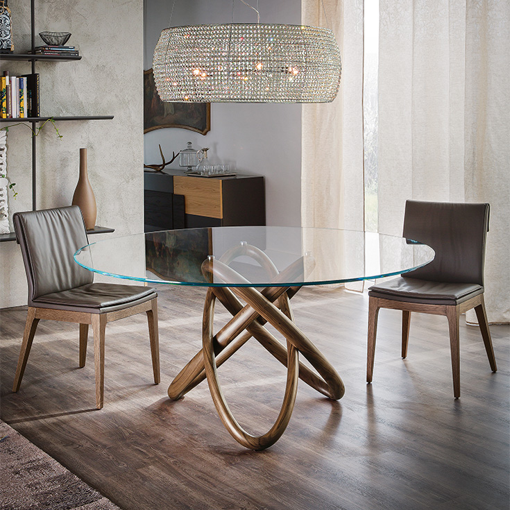 Comedor moderno con mesa redonda de cristal, dos sillas marrones y lámpara colgante de mimbre.