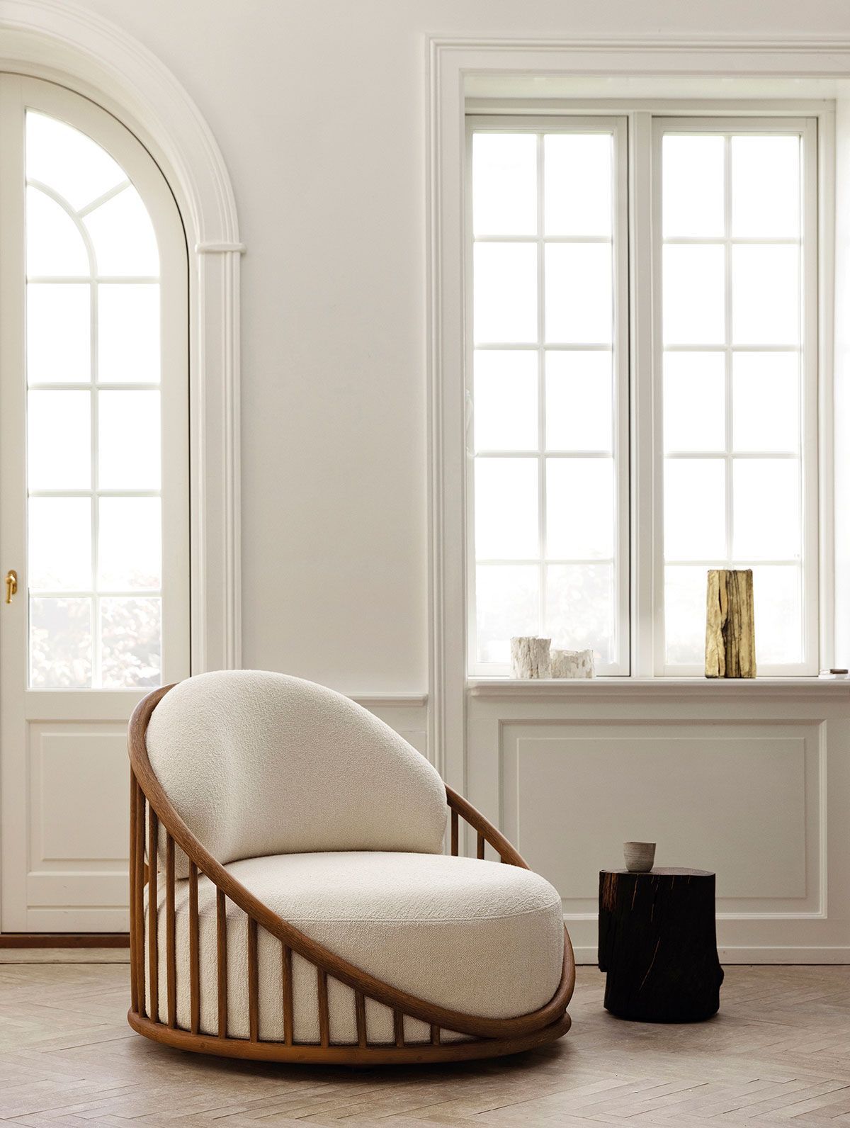 Silla acogedora de color crema con estructura de madera en una habitación blanca y luminosa junto a grandes ventanales.