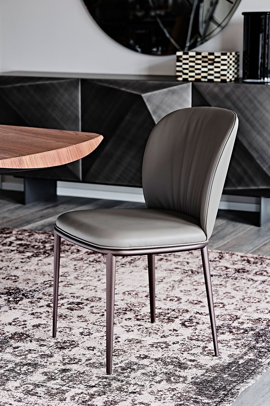 Silla moderna tapizada en gris con patas finas de metal sobre una alfombra estampada en una habitación con estilo.