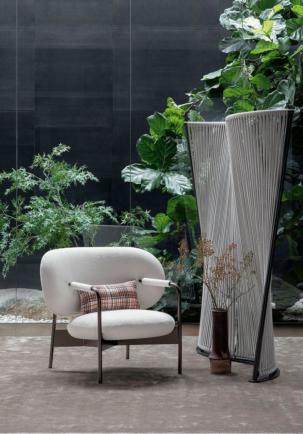 Patio minimalista con una silla color crema, un cojín estampado y una maceta alta junto a una exuberante vegetación.