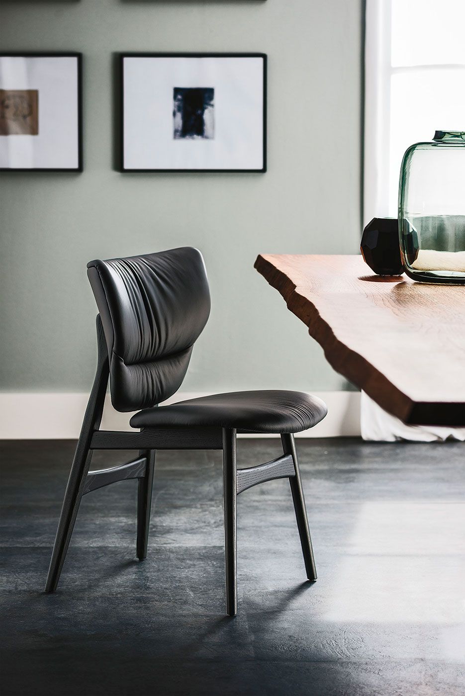 Silla negra en un comedor moderno junto a una mesa de madera y un cuadro enmarcado en la pared.