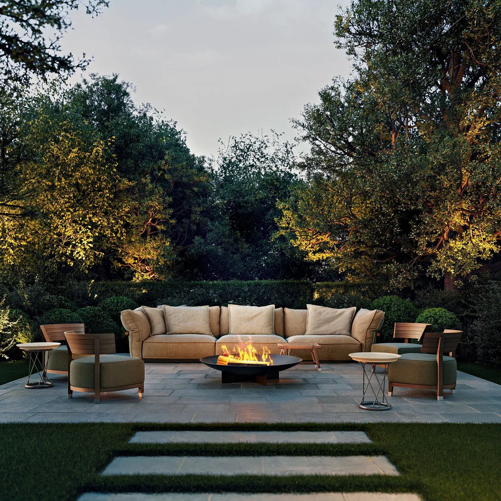 Patio exterior moderno con sofá modular beige, fogata y tumbonas entre árboles al atardecer.