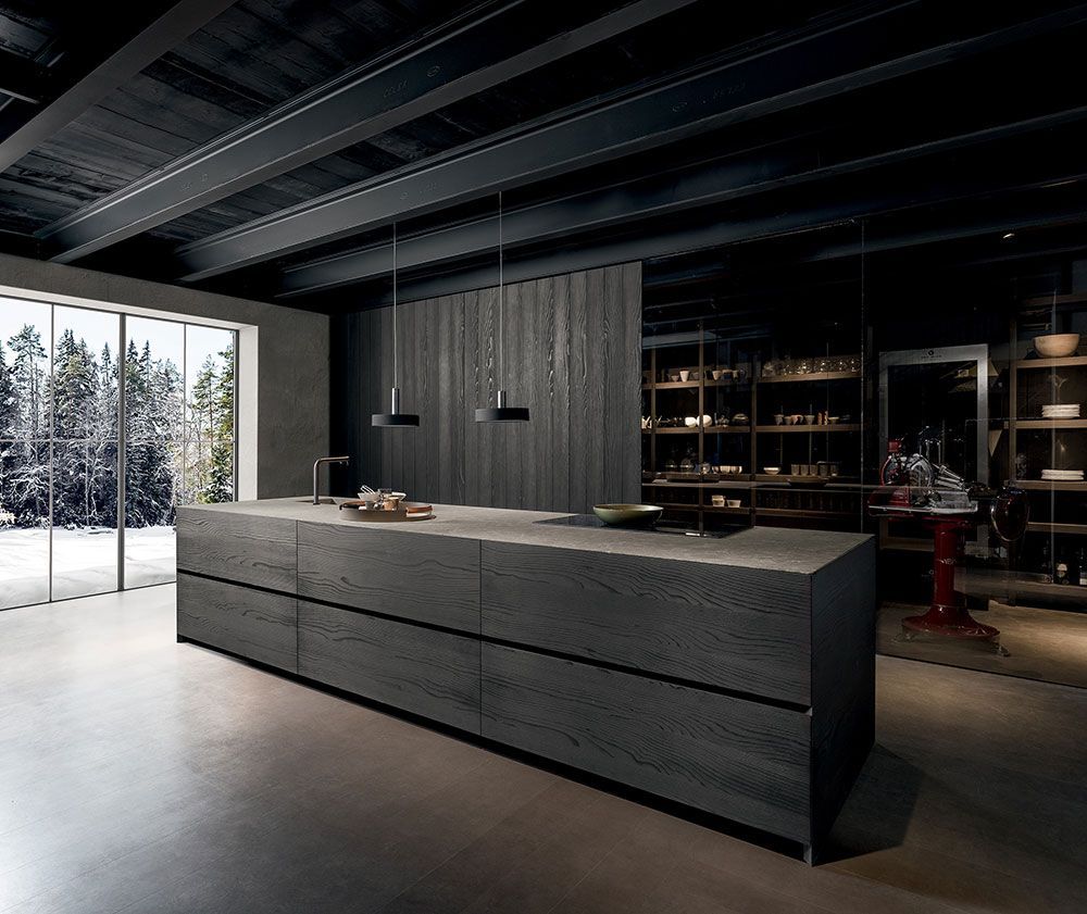 Cocina moderna de tonos oscuros con una gran isla, estanterías abiertas y árboles nevados visibles a través de una ventana