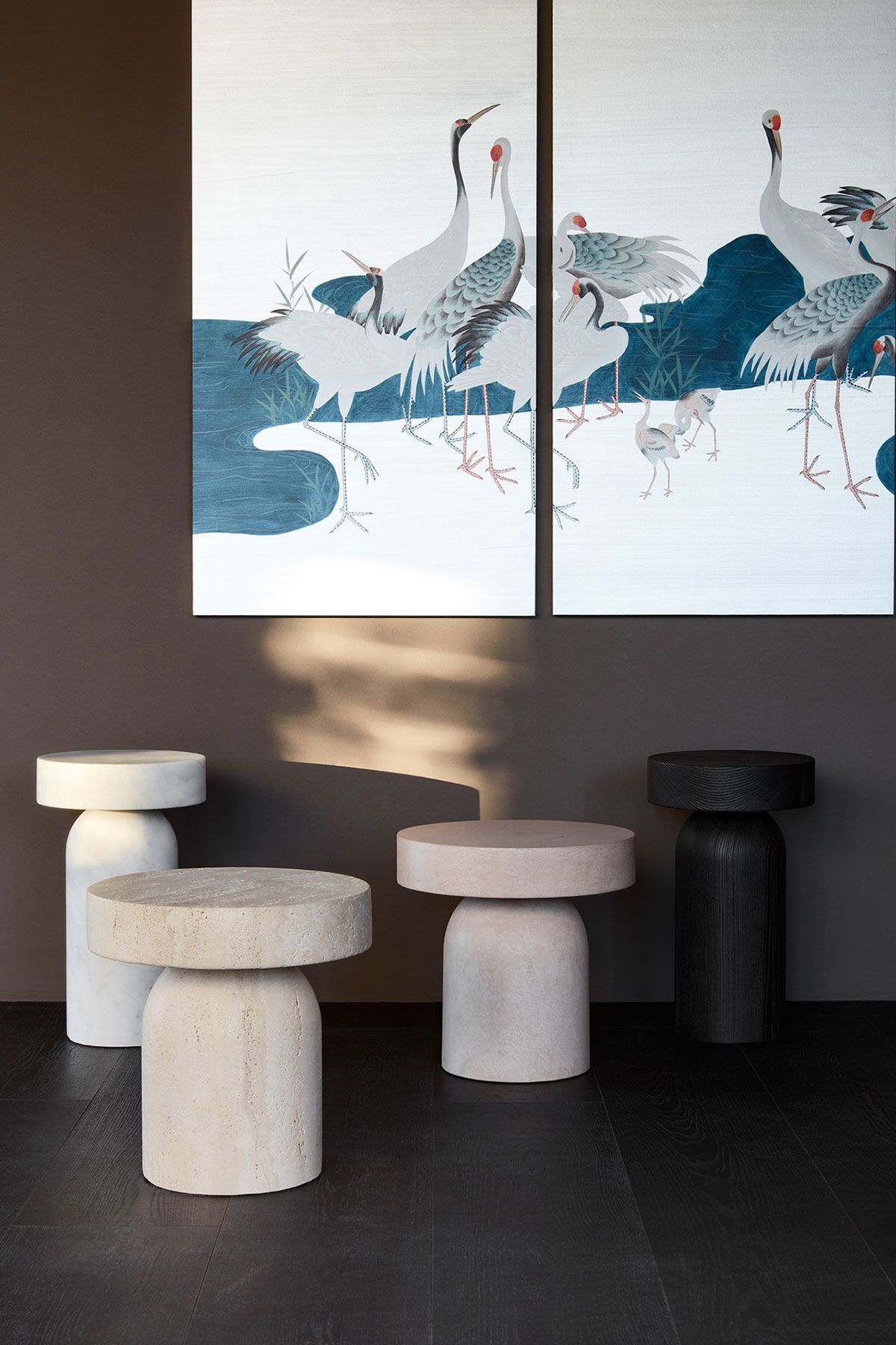 Habitación minimalista con una obra de arte abstracta de una grulla y taburetes de piedra esculturales sobre un suelo oscuro.