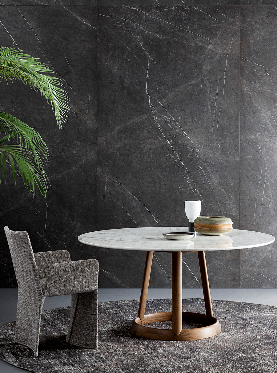 Silla moderna y mesa redonda con decoración en una habitación minimalista junto a una pared oscura texturizada.