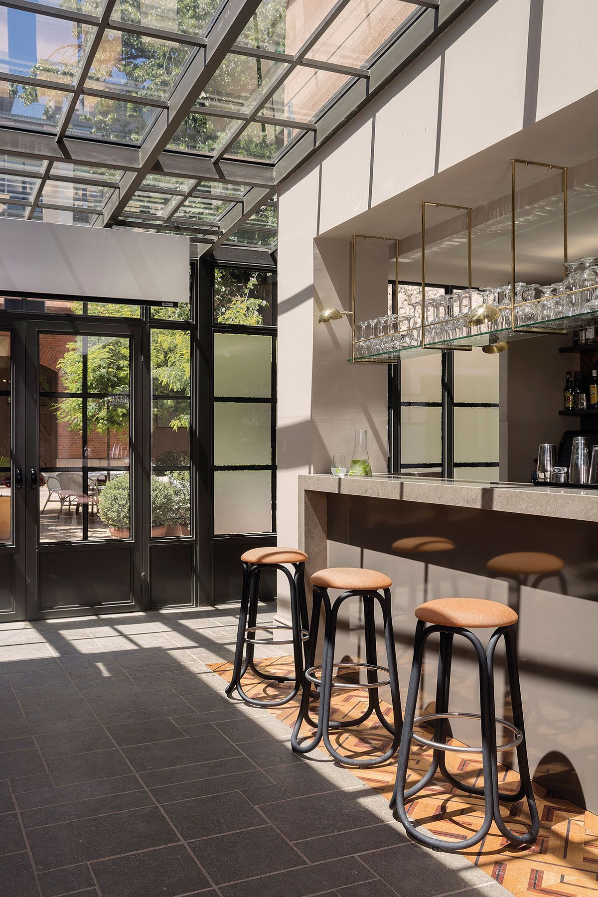 Cafetería luminosa y moderna con techo de cristal, barra y taburetes junto a la entrada.
