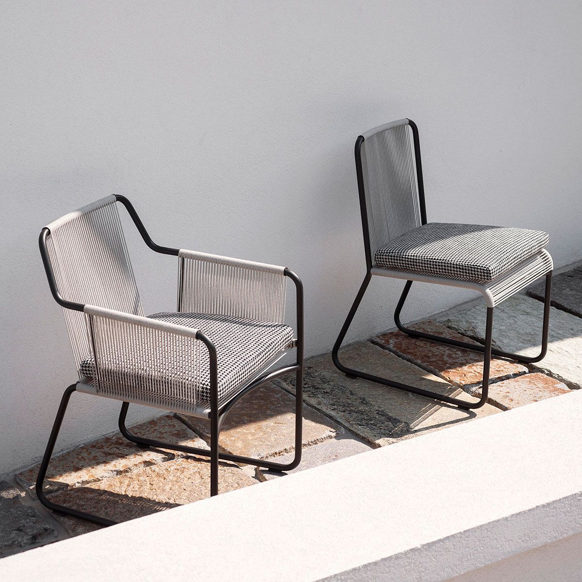 Dos sillas modernas de mimbre con estructura de metal negro en un luminoso patio al aire libre.