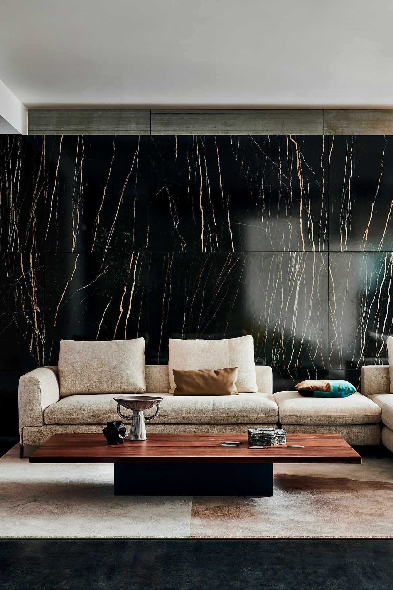 Sala de estar moderna con sofá beige, mesa de centro de madera y pared decorativa de mármol oscuro con vetas doradas.