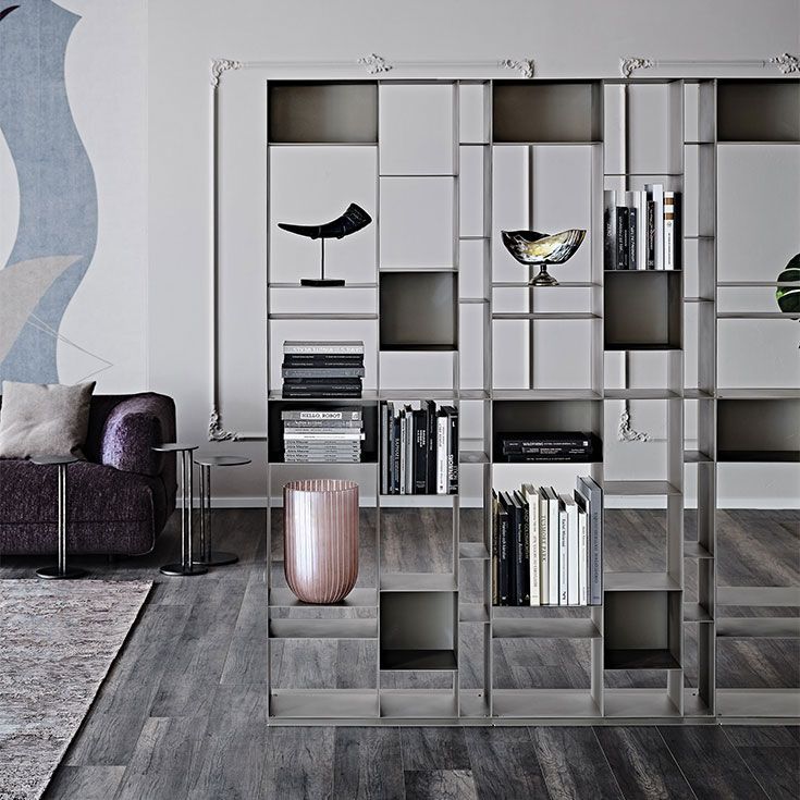 Salón moderno con estantería geométrica y objetos decorativos, junto a un sofá y una alfombra.
