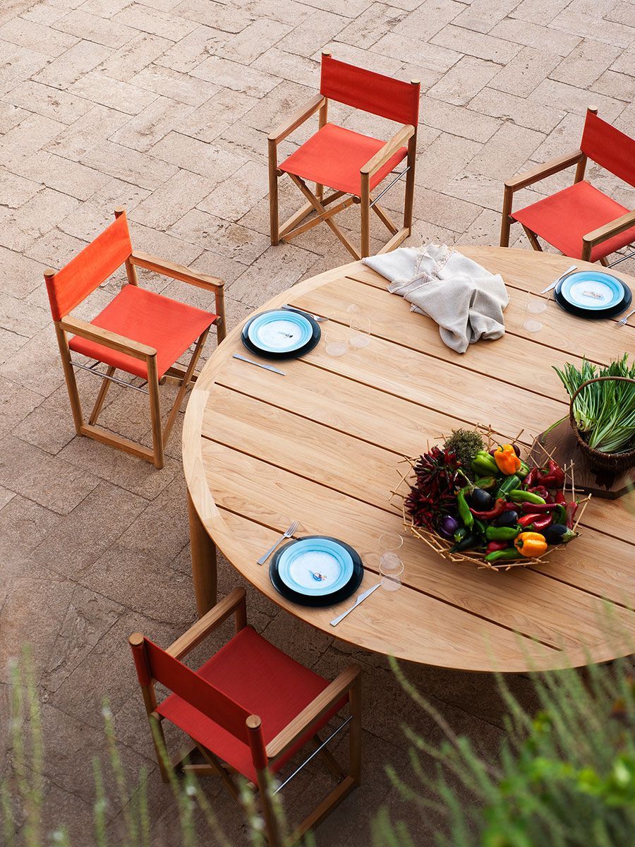 Patio exterior con una mesa redonda de madera, sillas rojas y platos puestos para comer.