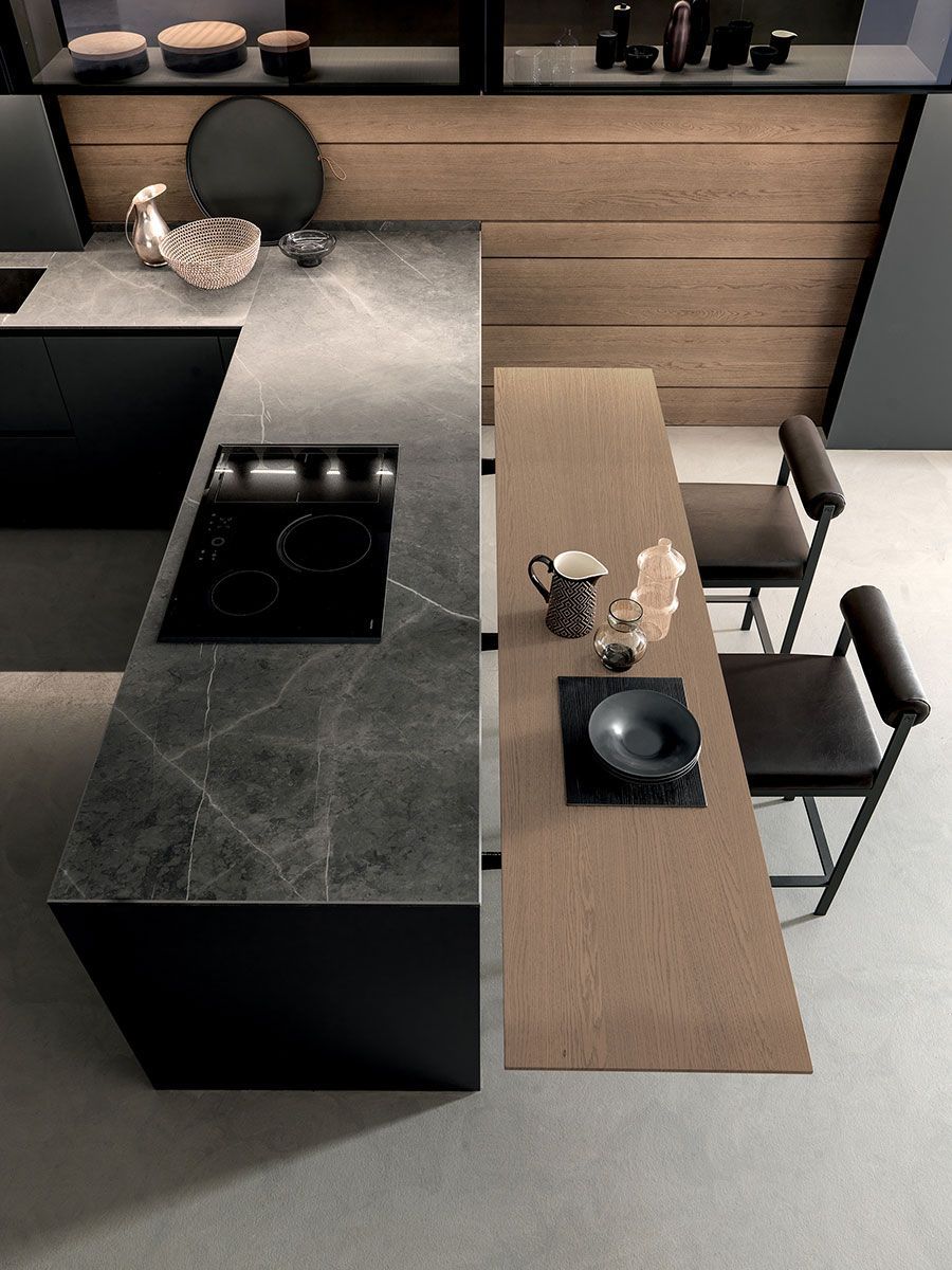 Cocina moderna con isla negra, armarios de madera y dos taburetes junto a una barra de comedor.
